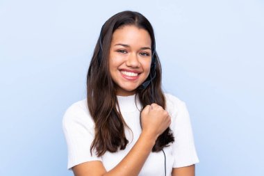 Genç tele pazarlamacı Kolombiyalı kadın mavi arka planda zaferi kutluyor.