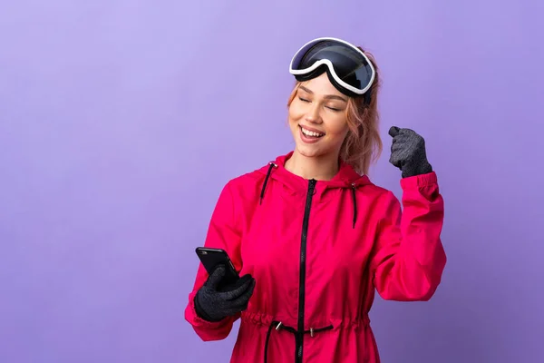 一个滑雪板女孩 戴着雪板眼镜 背景是紫色的 手机在胜利的位置上 — 图库照片