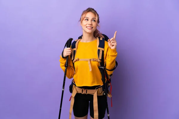 一个年轻姑娘 背着背包 带着远足的杆子穿越孤立的紫色背景 提出了一个很好的主意 — 图库照片