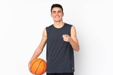 Yakışıklı genç basketbolcu izole duvarda basketbol oynuyor ve ön tarafı işaret ediyor.