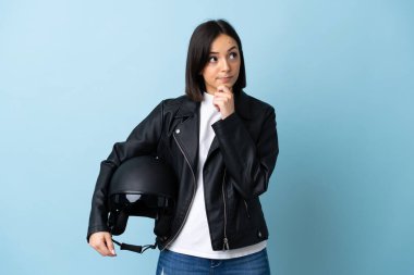 Mavi arka planda motosiklet kaskı tutan bir kadın var.