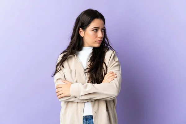 Young caucasian woman isolated on purple background keeping the arms crossed