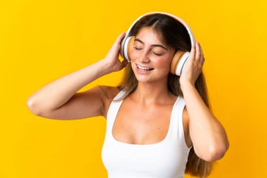Sarı arka planda izole edilmiş genç beyaz kadın müzik dinliyor.