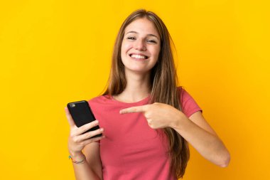 Sarı arka planda izole edilmiş cep telefonu kullanan genç bir kadın.