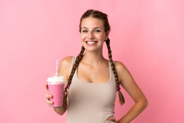 Çilekli milkshake 'i olan genç bir kadın pembe arka planda izole edilmiş, kolları kalçasında ve gülümsüyor.