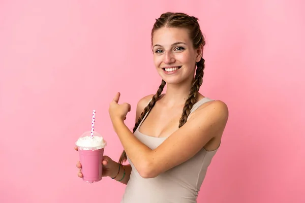 若いです女性とともにイチゴミルクセーキ隔離されたピンクの背景を指して — ストック写真