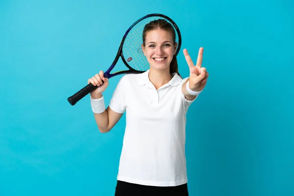 青の背景の笑顔と勝利のサインを示す上で隔離された若い女性テニス選手 — ストック写真