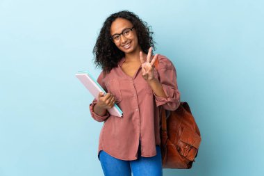 Mavi arka planda izole edilmiş genç kız mutlu ve parmaklarıyla üçe kadar sayıyor.