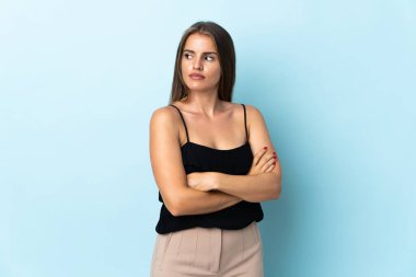 Genç Uruguaylı kadın mavi arka planda izole edilmiş, kollarını kavuşturuyor.