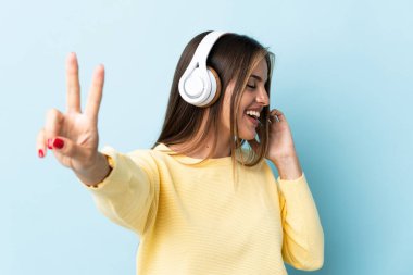 Genç Uruguaylı kadın mavi arka planda izole edilmiş müzik dinliyor ve şarkı söylüyor.