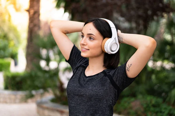 公園の屋外でヘッドフォンで音楽を聴く若いスポーツの白人女性 — ストック写真