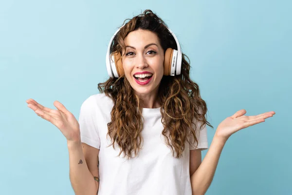 Joven Mujer Caucásica Aislada Sobre Fondo Azul Sorprendida Escuchando Música —  Fotos de Stock