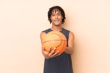 Genç Afrikalı Amerikalı adam bej arka planda izole edilmiş basketbol oynuyor.