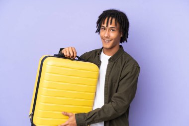 Genç Afro-Amerikan bir adam, mor arka planda izole edilmiş seyahat valiziyle tatilde.