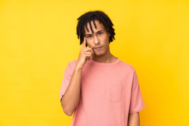 Genç Afrikalı Amerikalı bir adam sarı arka planda izole edilmiş bir fikir düşünüyor.