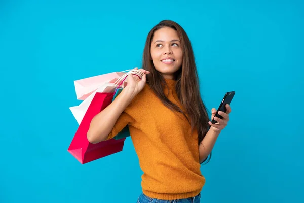 Joven Brasileña Sobre Fondo Azul Aislado Sosteniendo Bolsas Compras Teléfono —  Fotos de Stock