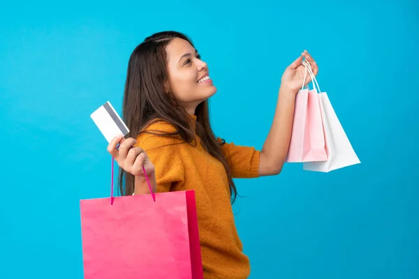 Junge Brasilianerin Vor Isoliertem Blauen Hintergrund Mit Einkaufstaschen Und Kreditkarte — Stockfoto