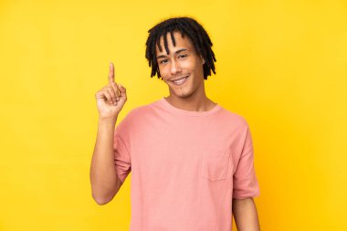 Genç Afrikalı Amerikalı adam sarı arka planda izole edilmiş ve en iyinin işareti olarak parmağını kaldırıyor.