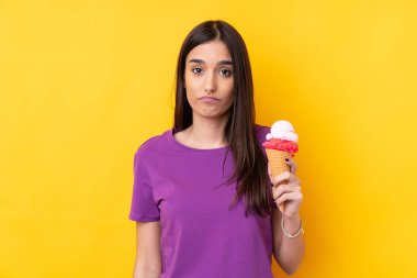 Kornet dondurmalı genç esmer kadın izole edilmiş sarı arka planda hüzünlü bir ifadeyle.