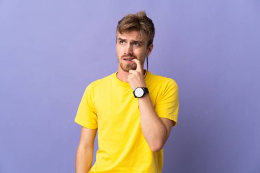 Genç, sarışın, mor arka planda yalnız, gergin ve korkmuş bir adam.