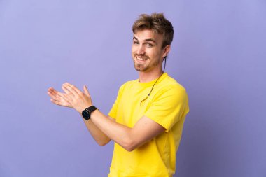 Mor arka planda izole edilmiş genç, sarışın adam alkışlıyor.