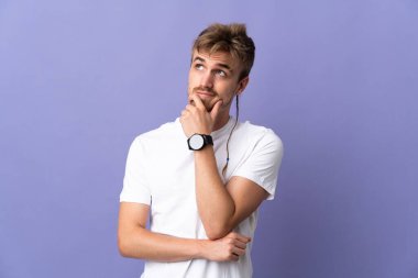 Genç yakışıklı sarışın adam mor arka planda izole edilmiş bir şekilde bakarken bir fikir düşünüyor.