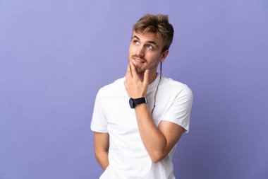 Genç yakışıklı sarışın adam mor arka planda izole edilmiş gülümserken yukarı bakıyor.