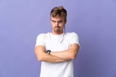 Genç yakışıklı sarışın adam, mor arka planda izole edilmiş, mutsuz bir ifadeyle.