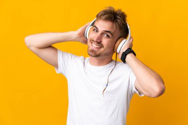 Sarı arka planda izole edilmiş yakışıklı sarışın adam müzik dinliyor.