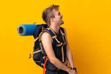 Sarı arka planda izole edilmiş büyük sırt çantalı genç dağcı yan pozisyonda gülüyor.