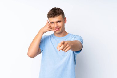 Soyutlanmış beyaz arka planda genç yakışıklı bir adam telefon jesti yapıyor ve ön tarafı işaret ediyor.