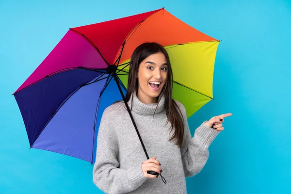 Joven Morena Sosteniendo Paraguas Sobre Una Pared Azul Aislada Apuntando — Foto de Stock