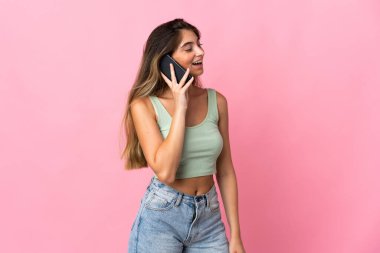 Pembe arka planda izole edilmiş genç beyaz kadın cep telefonuyla sohbet ediyor.