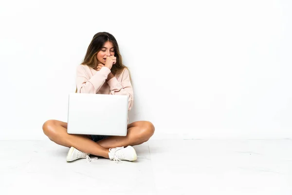 Young woman with a laptop sitting on the floor isolated on white background is suffering with cough and feeling bad