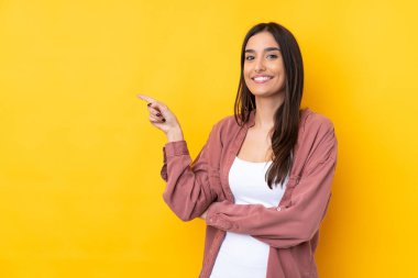 Genç esmer kadın, izole edilmiş sarı arka planda parmağını yana doğru gösteriyor.