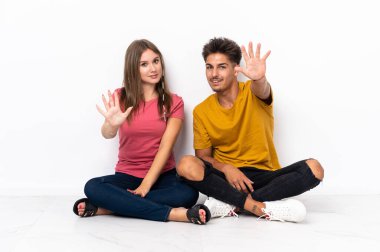 Yerde oturan genç çift beyaz arka planda tecrit edilmiş. Parmakları olan beş kişi saydım.