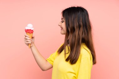 Genç esmer kadın elinde kornet dondurma tutarken mutlu bir ifadeyle izole edilmiş pembe arka planda.
