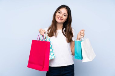Genç esmer kadın izole edilmiş mavi arka planda alışveriş torbaları tutuyor ve gülümsüyor.