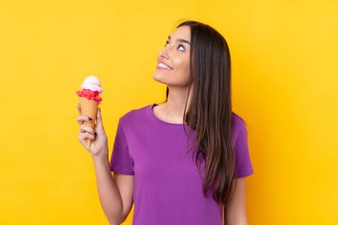 Kornet dondurmalı genç esmer kadın izole edilmiş sarı arka planda gülümserken yukarı bakıyor.