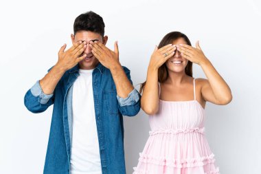 Beyaz arka planda izole edilmiş beyaz tenli genç çift elleriyle gözlerini kapatıyor.