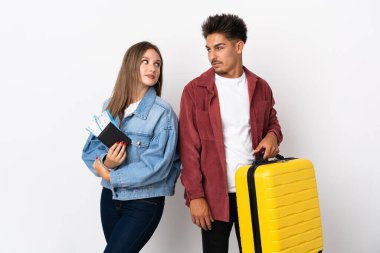 Mavi arka planda izole edilmiş bir bavul taşıyan gezgin çift gülümseyerek omzunun üzerinden bakıyor.