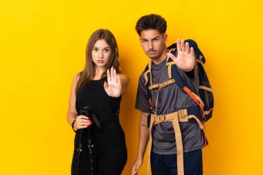 Sarı arka planda izole edilmiş büyük sırt çantalı genç dağcı çift yanlış düşünen bir durumu inkar etmeyi bırakıyorlar.