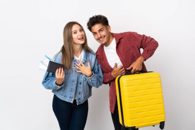 Mavi arka planda bir bavul taşıyan gezgin çift ellerini göğsüne koyup gülümsüyor.