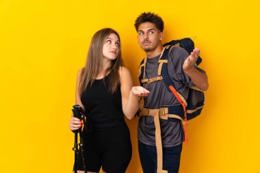 Sarı arka planda izole edilmiş büyük sırt çantalı genç dağcı çift omuzlarını kaldırırken önemsiz bir jest yapıyor.