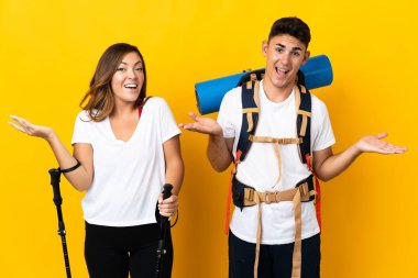 Sarı arka planda büyük sırt çantalı genç dağcı çift şok olmuş yüz ifadesine sahipler.