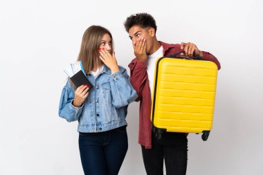 Gezgin çift mavi arka planda izole edilmiş bir bavul taşıyorlar uygunsuz bir şey söyledikleri için ağızlarını elleriyle kapatıyorlar.