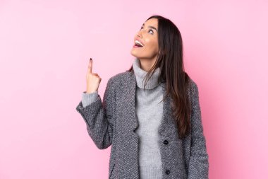 Soyutlanmış pembe arka planda genç esmer kadın yukarı bakıyor ve şaşırıyor.