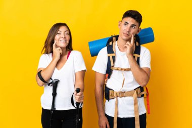 Sarı arka planda izole edilmiş büyük sırt çantalı genç dağcı çift yukarı bakarken bir fikir düşünüyorlar.