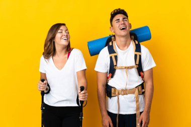 Sarı arka plana izole edilmiş büyük sırt çantalı genç dağcı çift gülüyor.