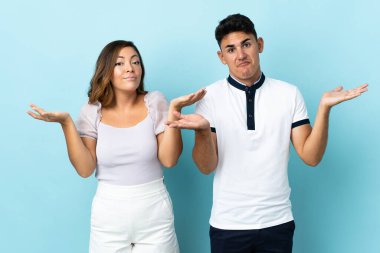 Kafkasyalı genç bir çift mavi arka planda izole edilmiş. Şüpheleri var ve kafası karışmış bir yüz ifadesi var.